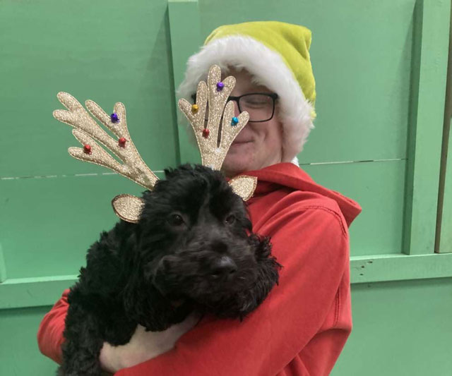 Canine coach Dale F in a festive elf hat, holding a curly black dog wearing reindeer antlers