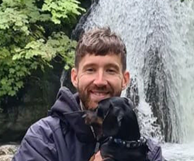 Canine coach Dale T holding a miniature dachshund in front of a waterfall