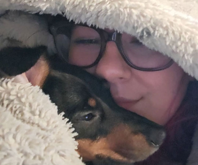 Canine coach Katie snuggled under a fluffy blanket with a black and tan dog