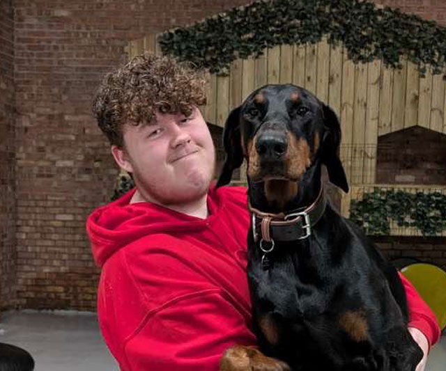 Milo, head of enrichment and play, hugging a Dobermann