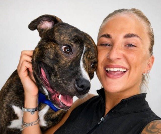 Sarah, groomer and owner of Barks & Bubbles, smiling cheek to cheek with a brindle dog